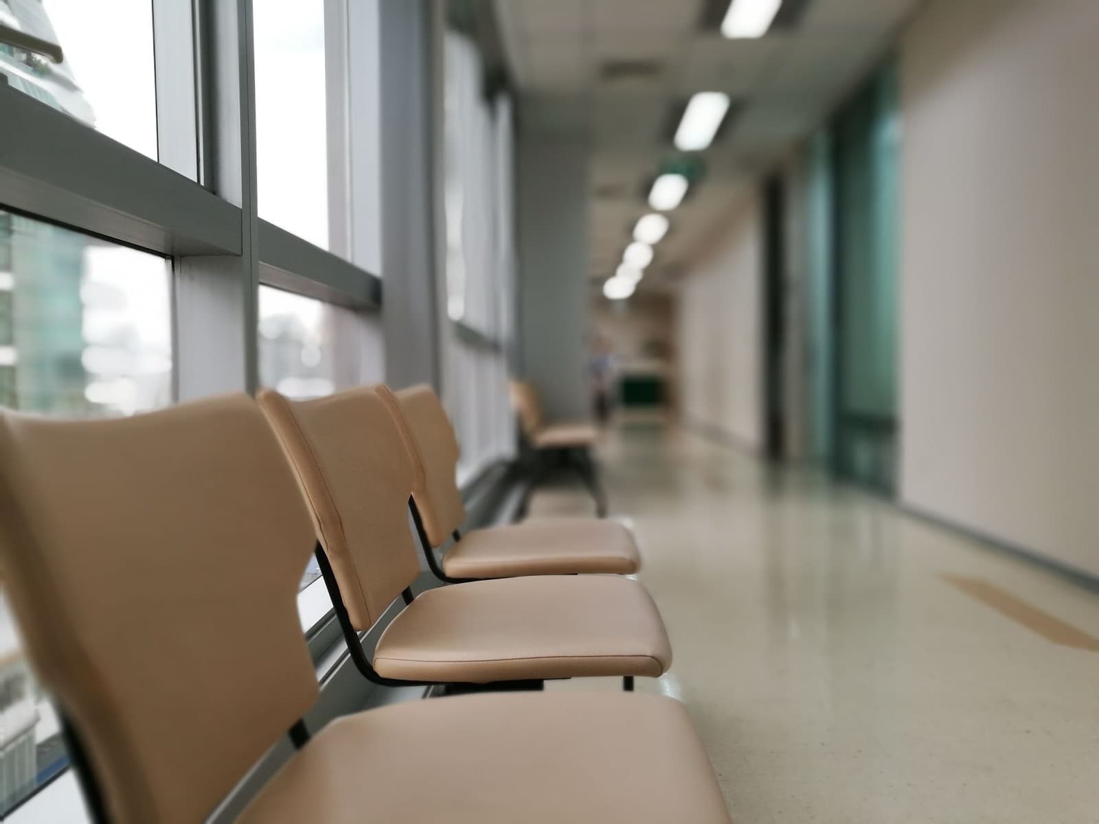 Rangée de sièges vides le long d'une baie vitrée dans un couloir de clinique